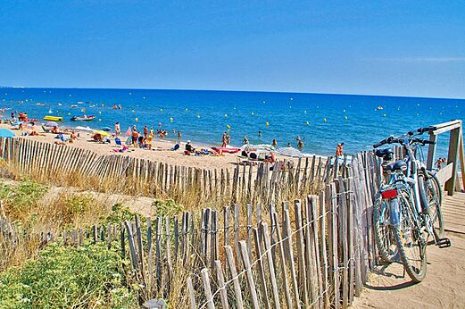 Playa de arena fina, bañistas y bicicletas en el camping CAPFUN Emeraude en Portiragnes (34).