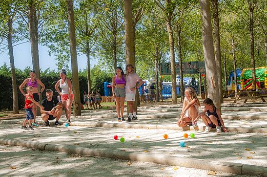 Familia jugando a la petanca en una cancha sombreada en el camping CAPFUN Emeraude en Portiragnes (34).