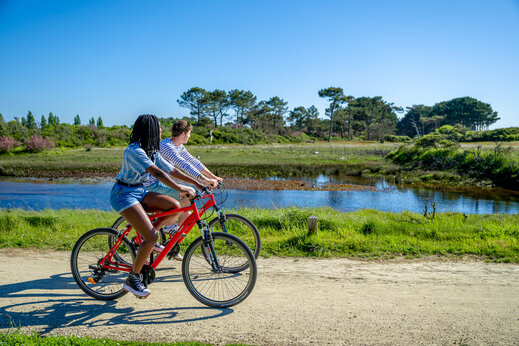 Dos personas en bicicleta por sendero de tierra junto a estanque, en camping CAPFUN Grand Large en FOUESNANT (29).