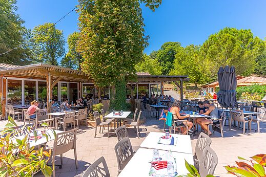 Terraza soleada del restaurante con clientes en el camping CAPFUN Imbours en LARNAS (07).