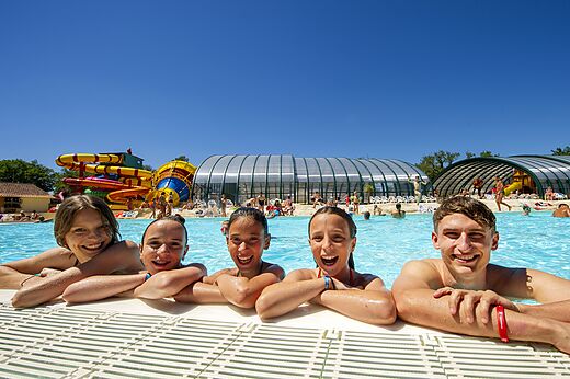Familia sonriente en la piscina con toboganes en el camping CAPFUN Imbours en LARNAS (07).