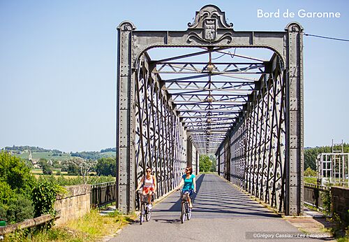 Dos personas en bicicleta sobre puente metálico cerca del río Garona, Bazas.