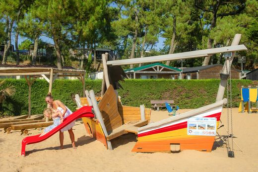 Zona de juegos con barco de madera, tobogán y niños en el camping CAPFUN Prises en La TRANCHE SUR MER (85).