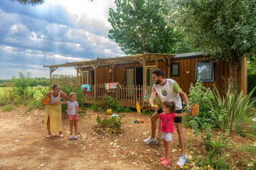 Familia jugando frente a un Mobil-home con terraza en el camping CAPFUN Prises en La TRANCHE SUR MER (85).