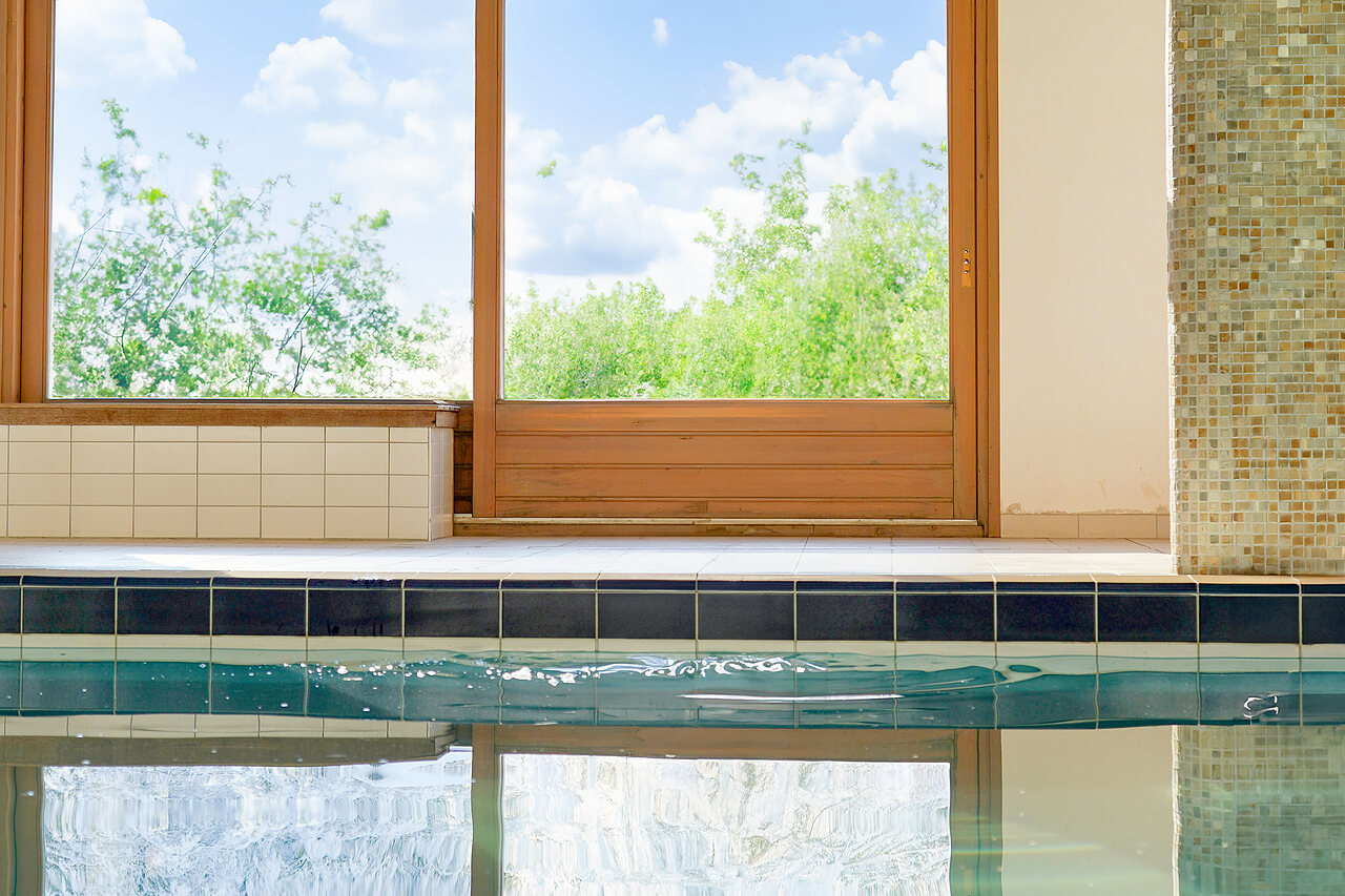 Borde de piscina cubierta con grandes ventanales a la naturaleza en el camping CLICOCHIC Alpes Lodges en Pralognan la Vanoise (73).