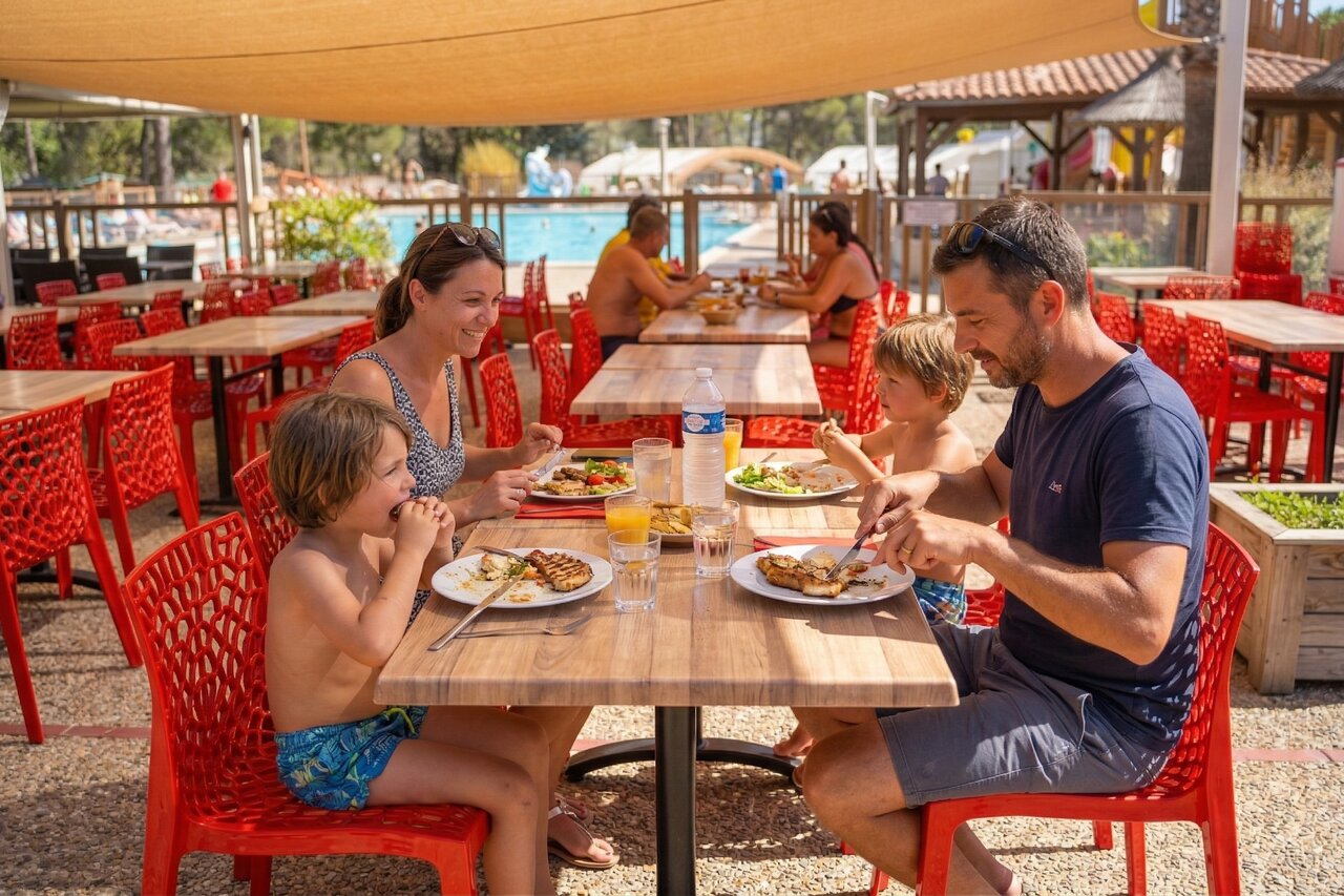 Familia almorzando en restaurante exterior junto a la piscina en camping CAPFUN Arbois du Castellet en LE CASTELLET (83).