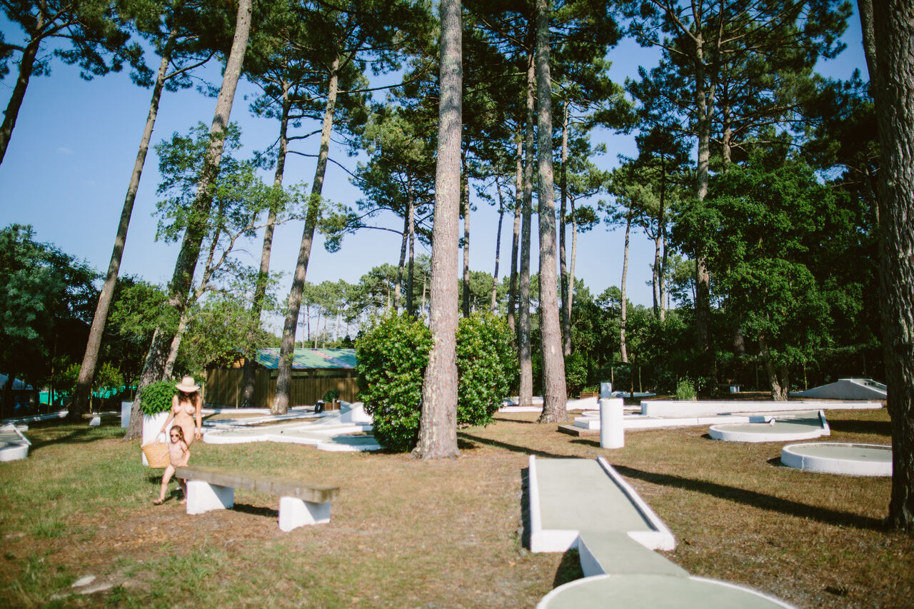 Campo de minigolf sombreado bajo pinos con familia en el camping LIBRANOO Naturiste Arnaoutchot en Veille-Saint-Girons, Landes, Francia.