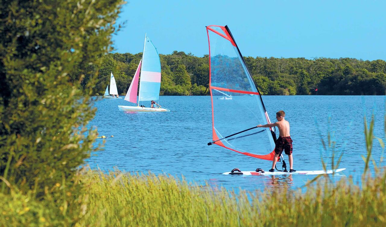 Joven practicando windsurf y veleros en el lago del camping LIBRANOO Naturiste Arnaoutchot, Landas, Francia.