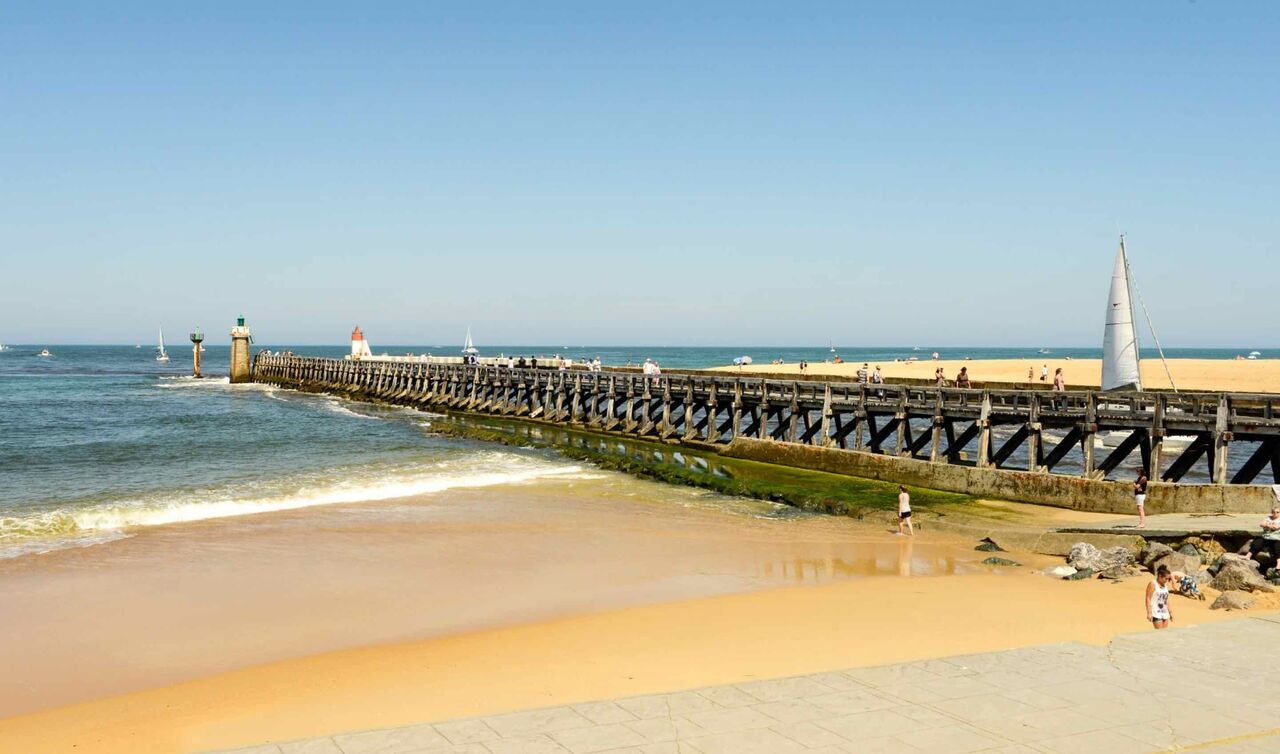 Playa de arena, muelle de madera, veleros en el camping LIBRANOO Naturiste Arnaoutchot.