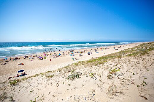 Playa de arena fina con bañistas y sombrillas en el camping LIBRANOO Naturiste Arnaoutchot en Veille-Saint-Girons, Landes, Francia.