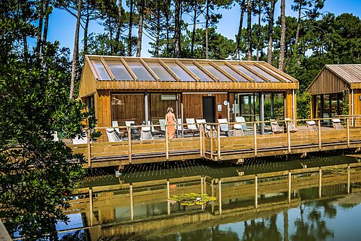 Edificio spa de madera con terraza sobre el agua en el camping LIBRANOO Naturiste Arnaoutchot en Veille-Saint-Girons, Landes, Francia.