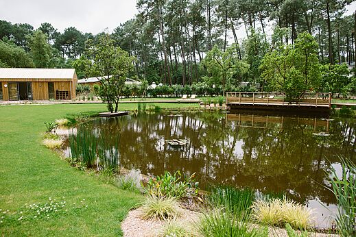 Estanque natural, vegetación y edificios de madera en el camping LIBRANOO Naturiste Arnaoutchot.