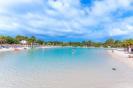 Gran piscina laguna con playa de arena y palmeras en el camping CAPFUN Atlantique Parc en Les Mathes / La Palmyre (17).