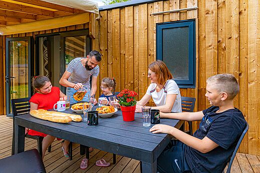 Familia comiendo en terraza de Mobil-home en camping CAPFUN Aube en Deltebre, Tarragona.