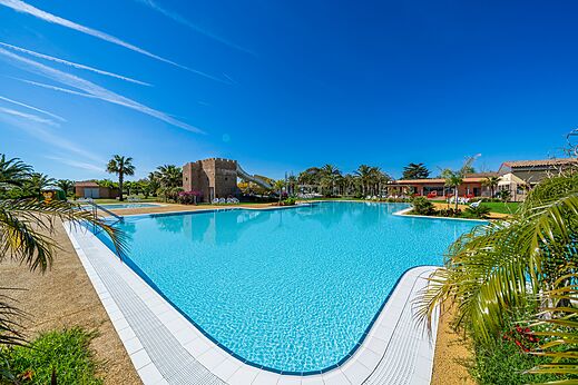 Gran piscina exterior con tobogán y palmeras en el camping CAPFUN Aube en Deltebre, Tarragona.