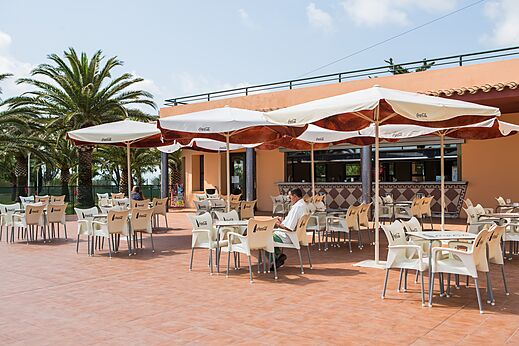 Terraza exterior del bar-restaurante con mesas y sombrillas en el camping CAPFUN Aube.