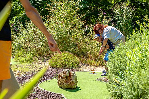 Niño y adulto jugando al minigolf en el campo del camping CAPFUN Aubrèdes en Puget sur Argens (83).