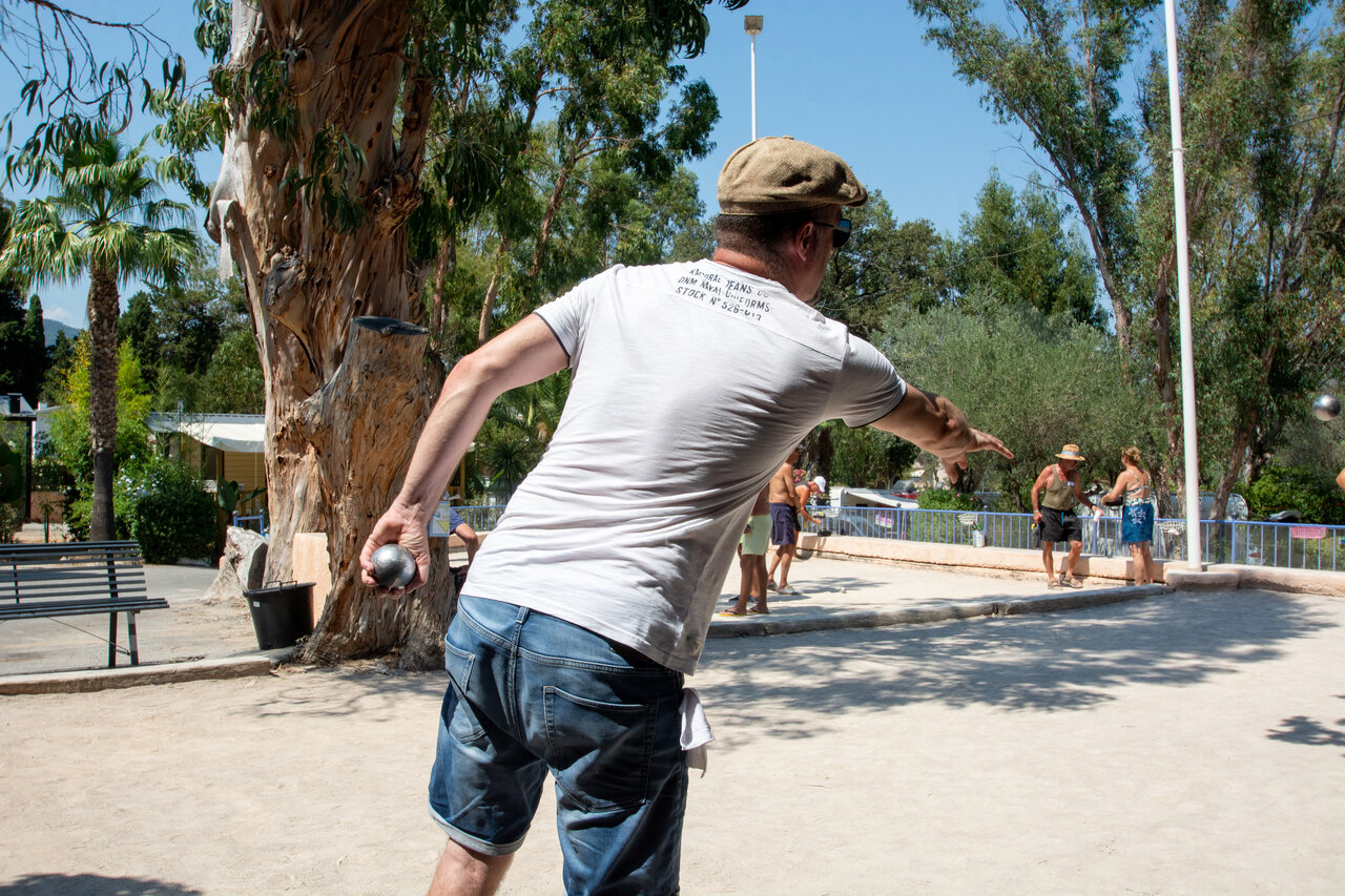 Hombre jugando a la petanca en cancha sombreada en el camping CLICOCHIC Baie de Cavalaire en Cavalaire-sur-Mer (83).