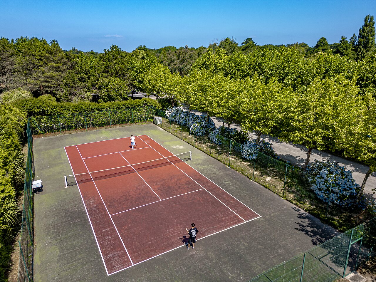 Cancha de tenis exterior con jugadores en el camping CLICOCHIC Baie de Douarnenez (29).