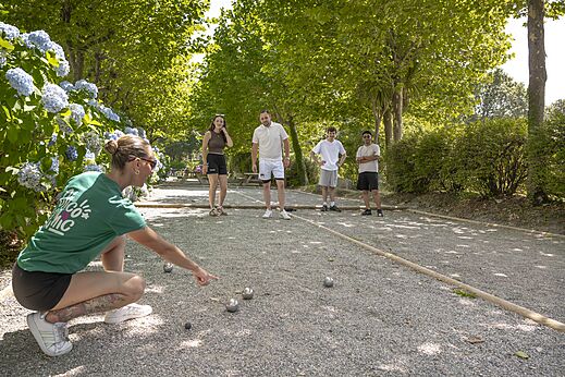 Pista de petanca sombreada con jugadores en el camping CLICOCHIC Baie de Douarnenez en Poullan-sur-Mer.