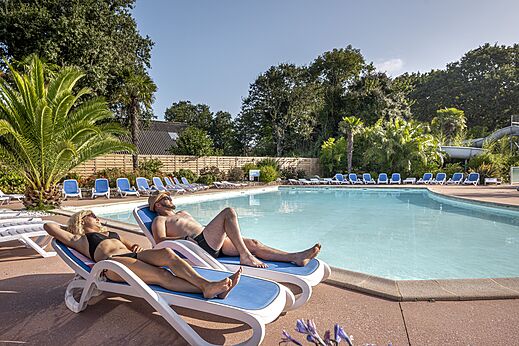 Piscina exterior, sillas y veraneantes en el camping CLICOCHIC Baie de Douarnenez.