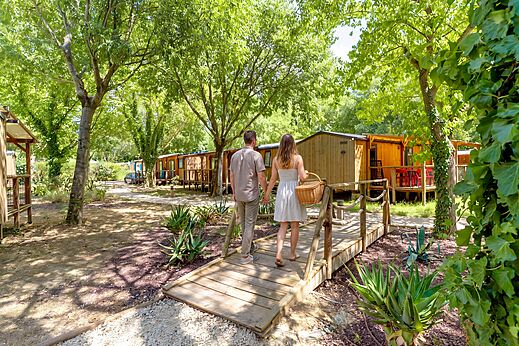 Pareja caminando hacia Mobil-homes sombreados en el camping CAPFUN Bastide en Nîmes (30).