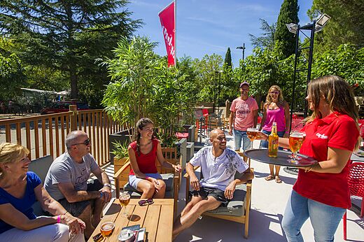Terraza de bar exterior con clientes y camarera en camping CAPFUN Bastide Nîmes (30).