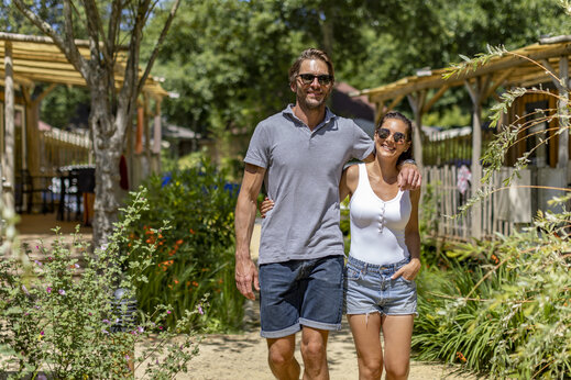 Pareja sonriente paseando por sendero verde en el camping CAPFUN Beauregard en MORNAS (84).