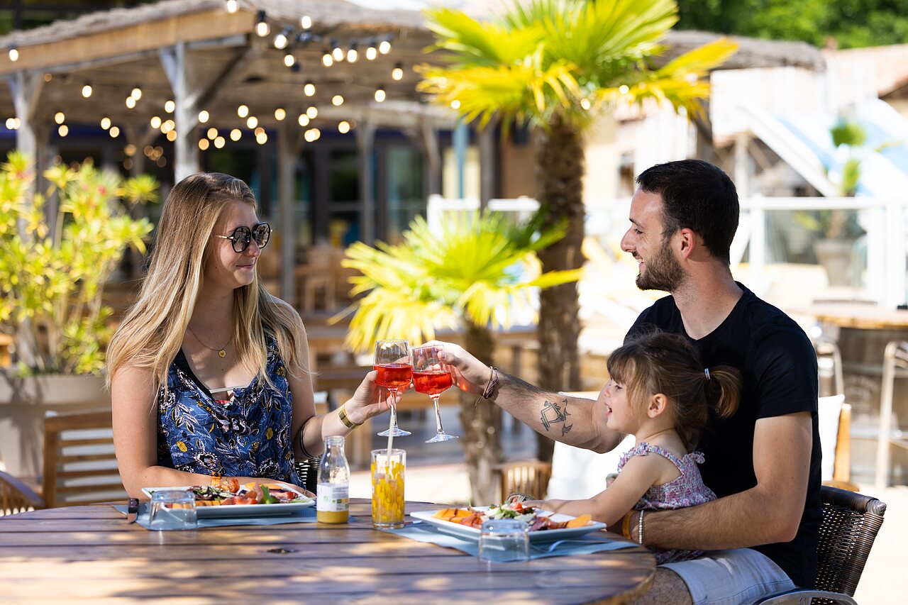Familia feliz cenando en la terraza del restaurante del camping CLICOCHIC Bimbo en BISCARROSSE (40).