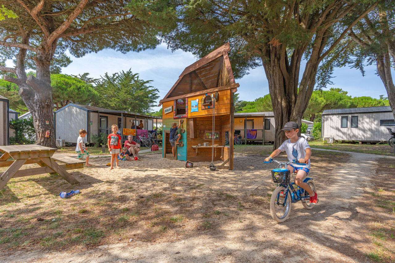 Zona de juegos con casita de madera, ni�os y mobil-homes en el camping CAPFUN Bonne Etoile en BOIS PLAGE EN RE (17).