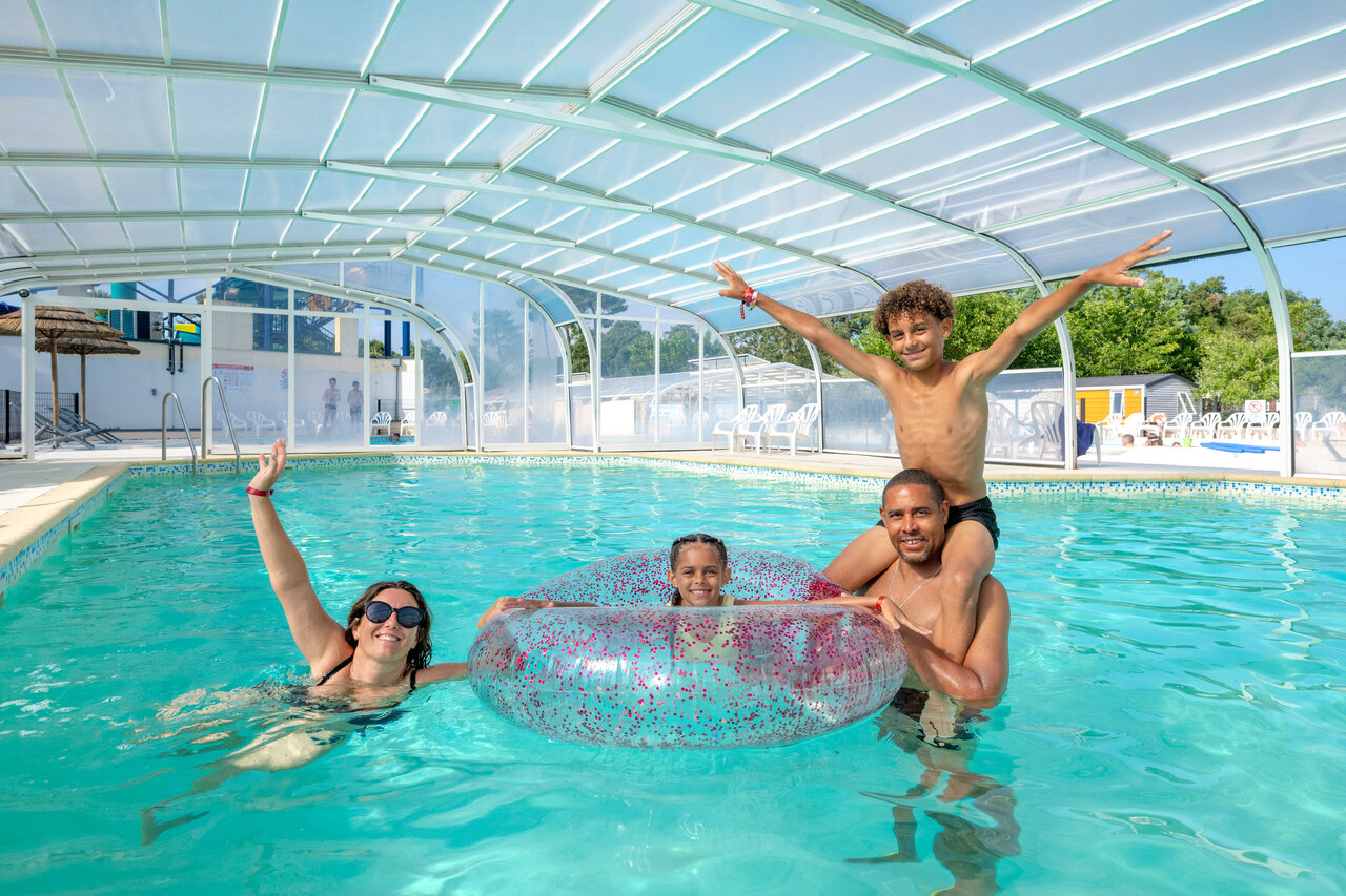 Familia sonriente disfrutando de la piscina cubierta en el camping VAGUES OCEANES Boudigau en LABENNE OCEAN (40).