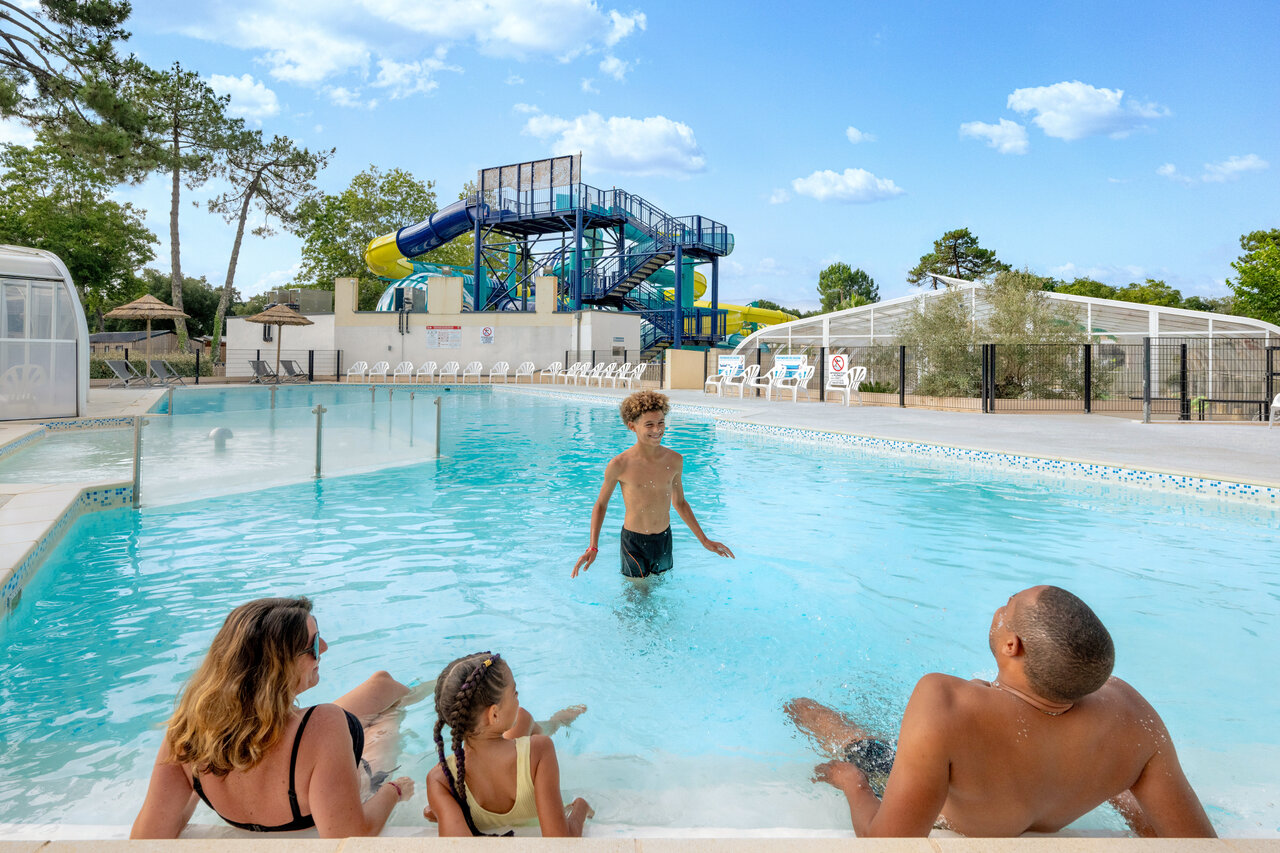 Familia disfrutando de la piscina exterior con toboganes en el camping VAGUES OCEANES Boudigau en LABENNE OCEAN (40).