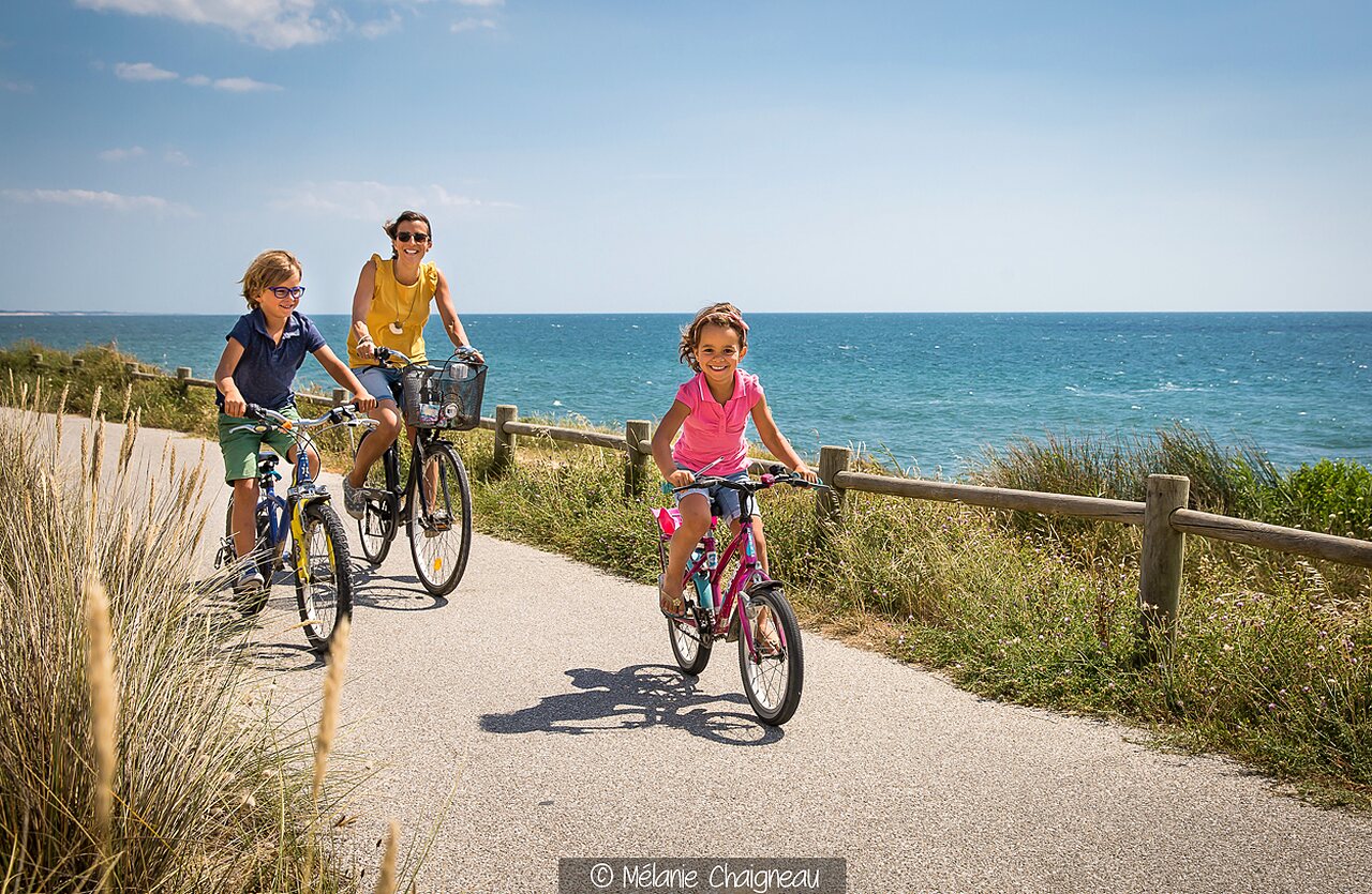 Familia en bicicleta por carril bici costero, mar, en el camping CLICOCHIC Brandais en Brem sur Mer.