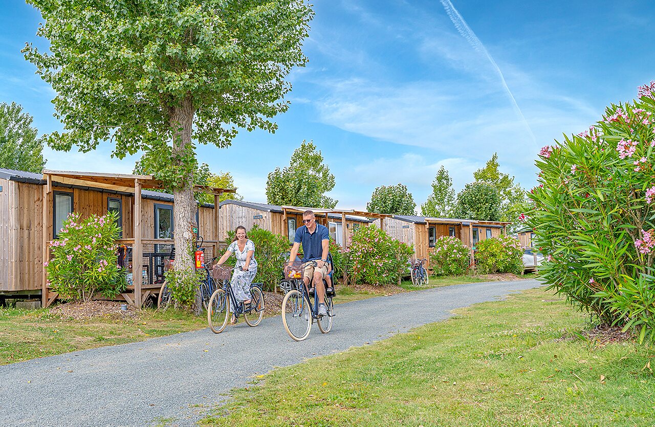 Pareja en bicicleta frente a Mobil-homes de madera en el camping CLICOCHIC Brandais.