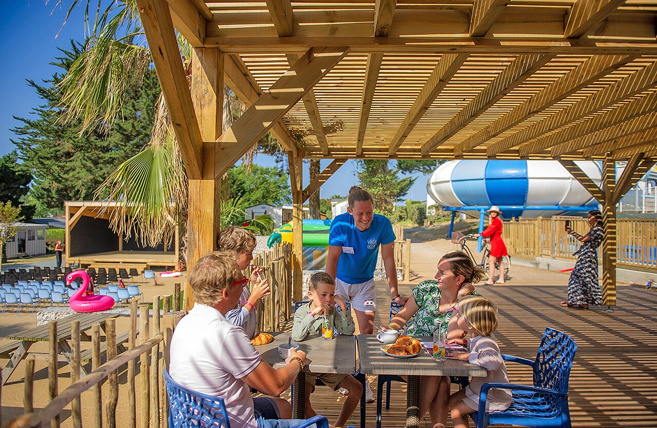 Familia desayunando bajo p�rgola, animador, escenario, tobog�n en camping CLICOCHIC Brandais en Brem sur Mer (85).