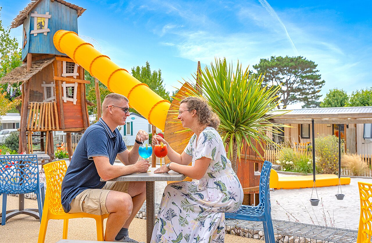 Tobog�n, pareja con bebidas y Mobil-homes en el camping CLICOCHIC Brandais en Brem sur Mer.