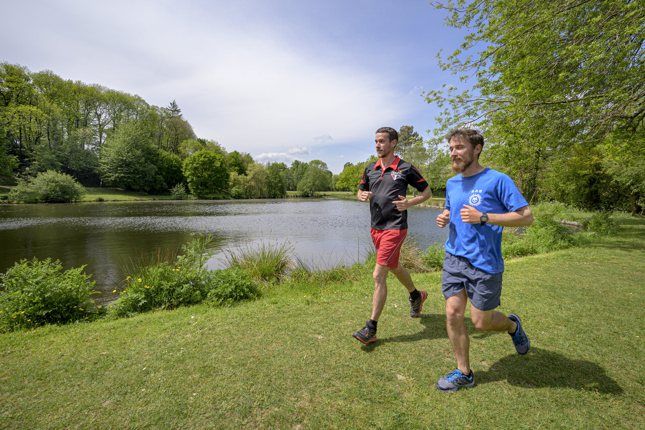 Dos hombres corriendo junto a un lago, entorno natural verde, en el camping CAPFUN Breteche en Les Epesses (85).