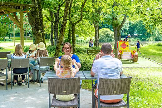 Familia comiendo en terraza exterior, juegos infantiles, camping CAPFUN Breteche en Les Epesses (85).
