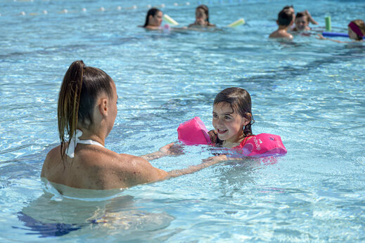 Niña sonriente con manguitos y adulto en la piscina del camping CAPFUN Breteche en Les Epesses (85).