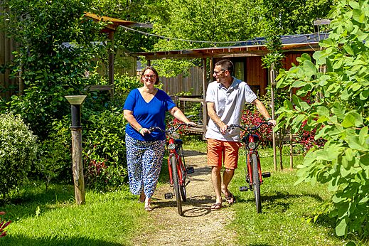 Pareja caminando con bicicletas rojas en sendero verde en camping CAPFUN Breteche en Les Epesses (85).