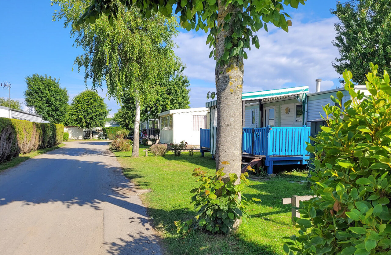 Mobil-homes con terrazas azules y camino arbolado en CLICOCHIC Brise de Cabourg.