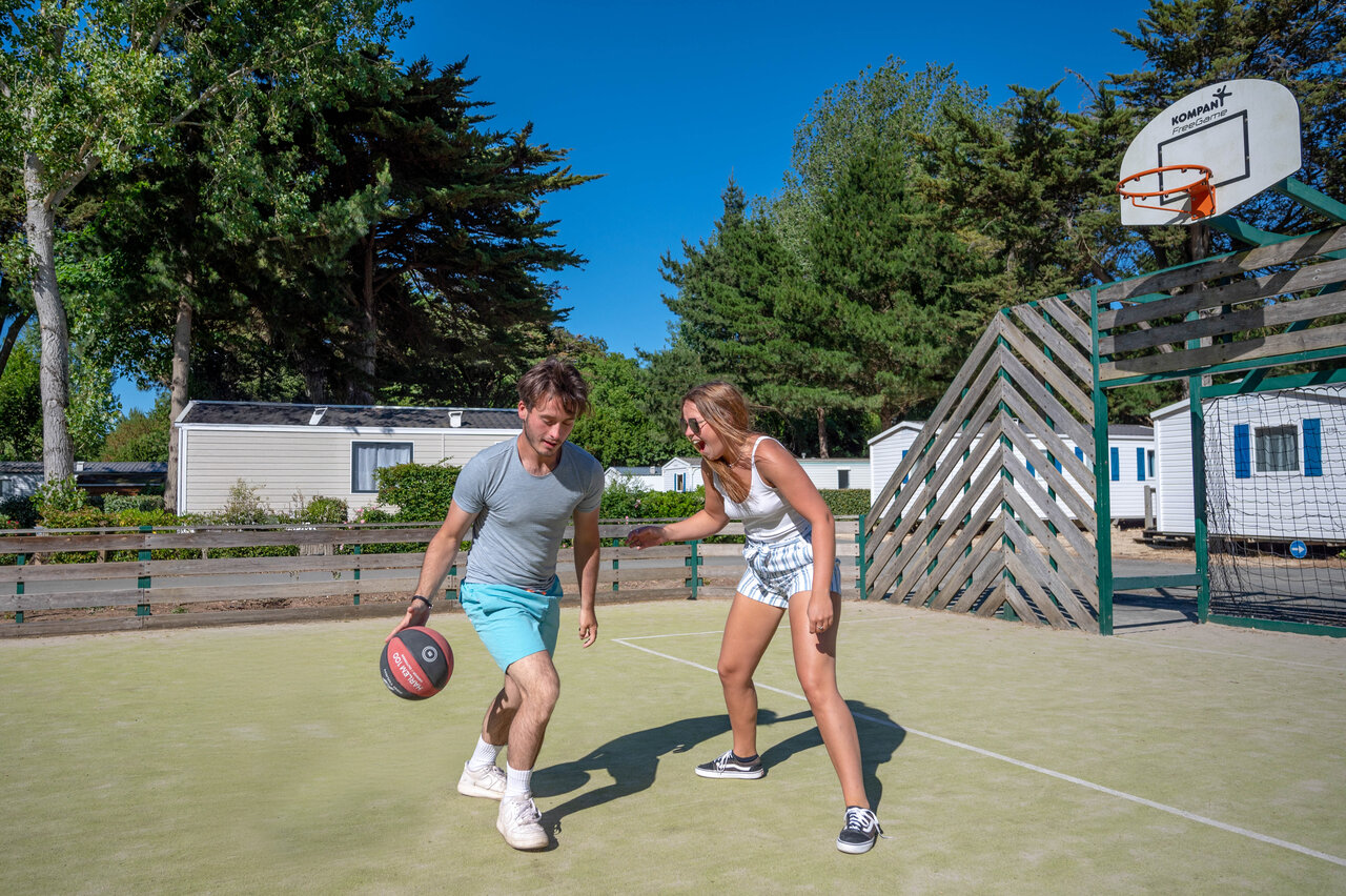 Pareja jugando baloncesto en cancha multideportiva en camping CLICOCHIC Cabanes d'Ol�ron.