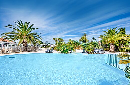 Piscina exterior soleada con palmeras en el camping CLICOCHIC Cabanes d Oléron en ST GEORGES D'OLERON