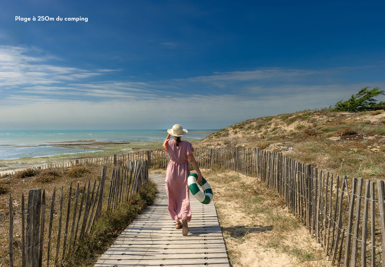 Mujer caminando por pasarela de madera hacia la playa en el camping CLICOCHIC Camp du Soleil en Ars-en-R� (17).