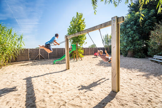 Dos niños juegan en columpios del parque infantil en el camping CLICOCHIC Camp du Soleil en Ars-en-Ré (17).
