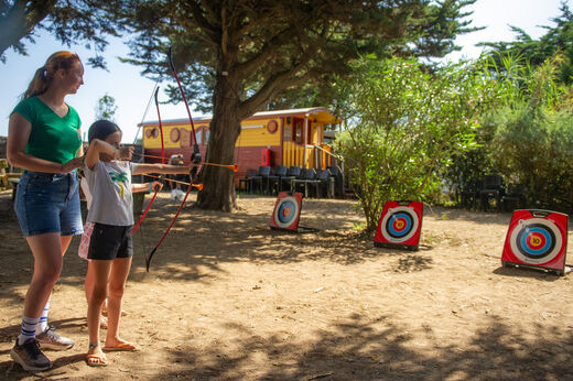 Niño practicando tiro con arco con monitor en el camping CLICOCHIC Camp du Soleil en Ars-en-Ré (17).