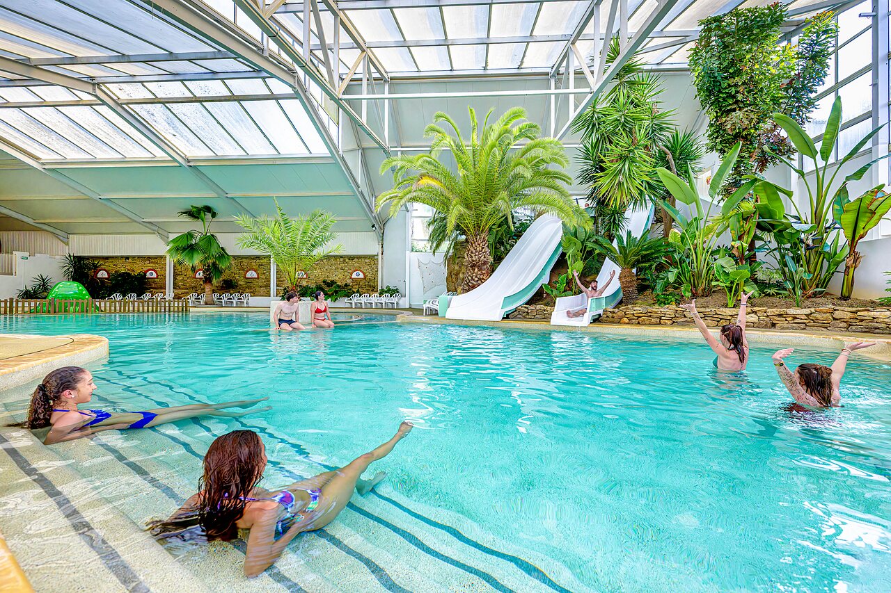 Piscina cubierta con toboganes y palmeras en el camping CAPFUN Cenic en PENESTIN (56).