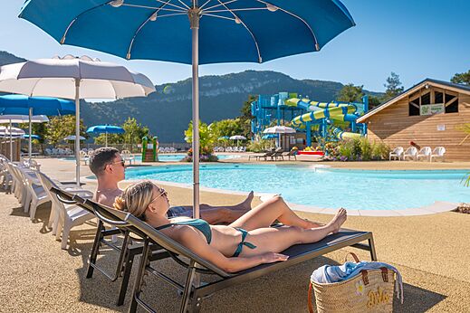 Piscina exterior, toboganes y pareja en sillas en el camping CLICOCHIC Chancia (01).