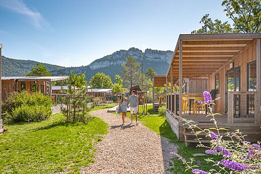 Mobil-homes de madera con terrazas y pareja paseando en el camping CLICOCHIC Chancia en Chancia (01).