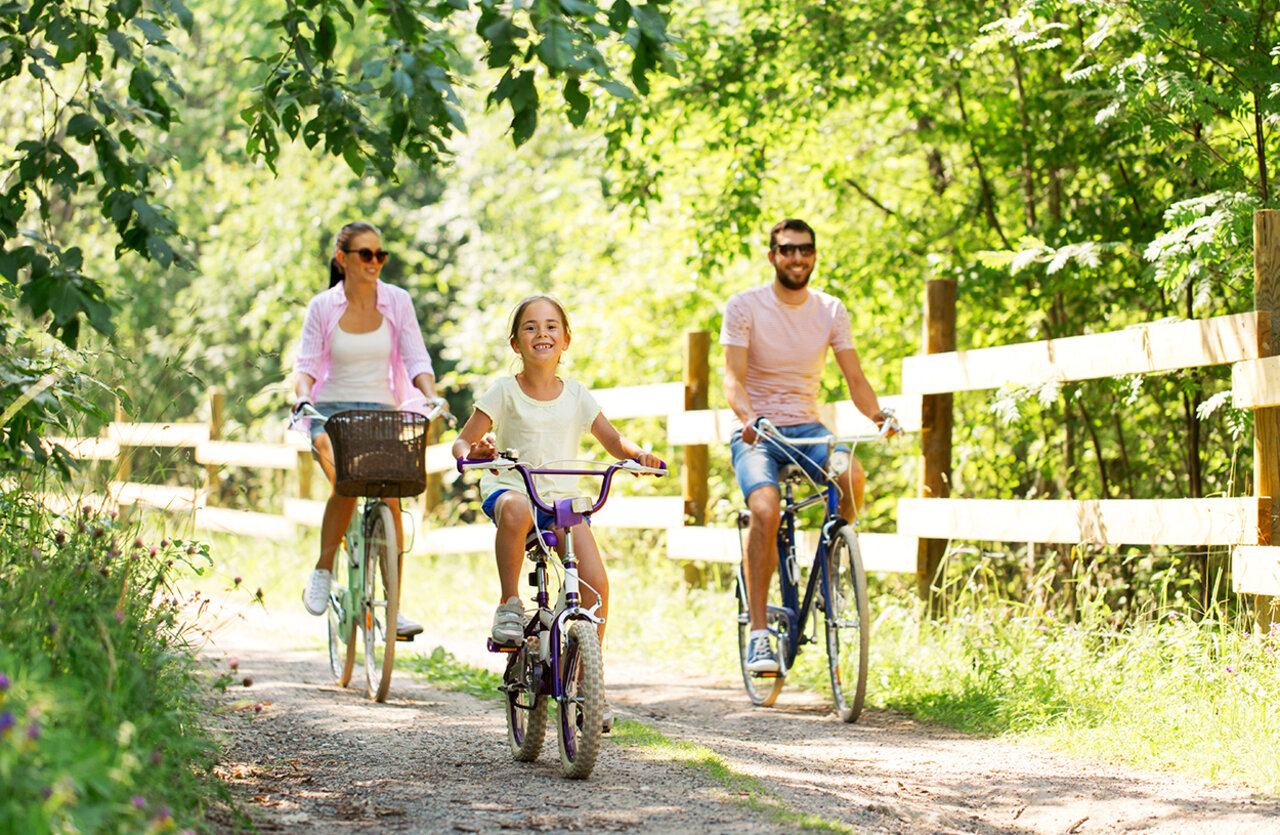 Familia en bicicleta por sendero arbolado en camping VAGUES OCEANES Domaine les Charmilles.